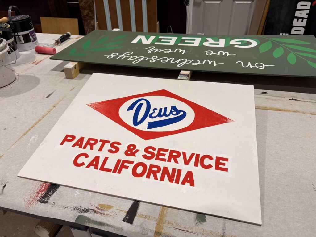 Hand-painted Deus Parts and Service California sign on a workbench