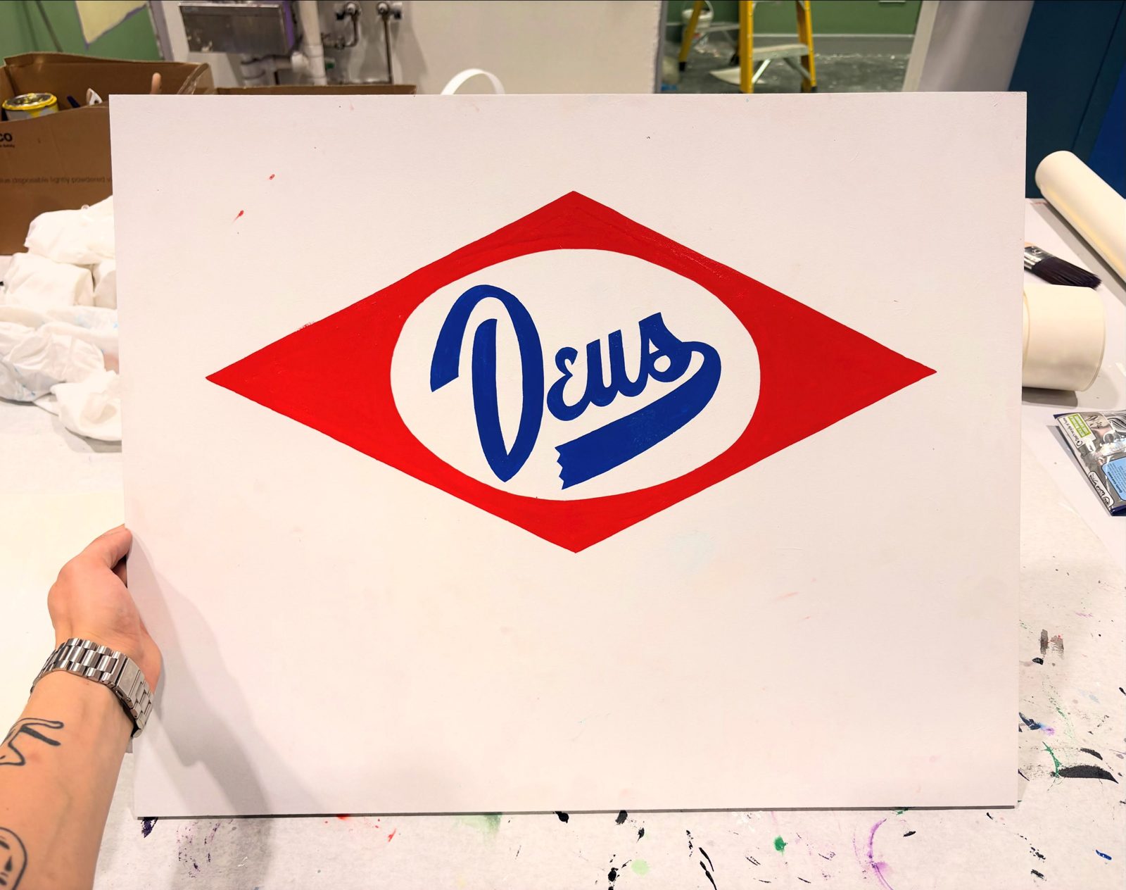 Hand-painted Deus sign with blue script inside a red diamond
