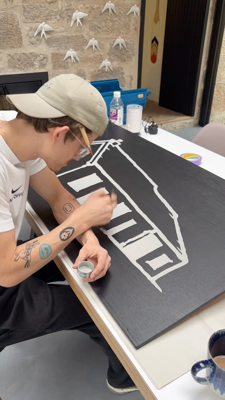 Torin hand-painting a white house illustration onto a black timber board Torin hand-painting a white house illustration onto a black timber board