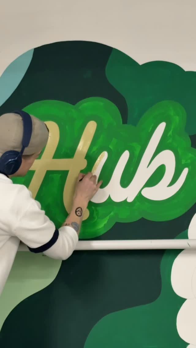 Torin hand-painting script lettering on a green office mural Torin hand-painting script lettering on a green office mural