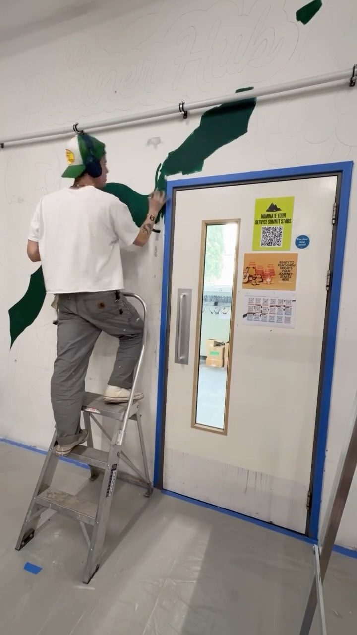 Torin on a step ladder blocking in the first green shapes of an office mural