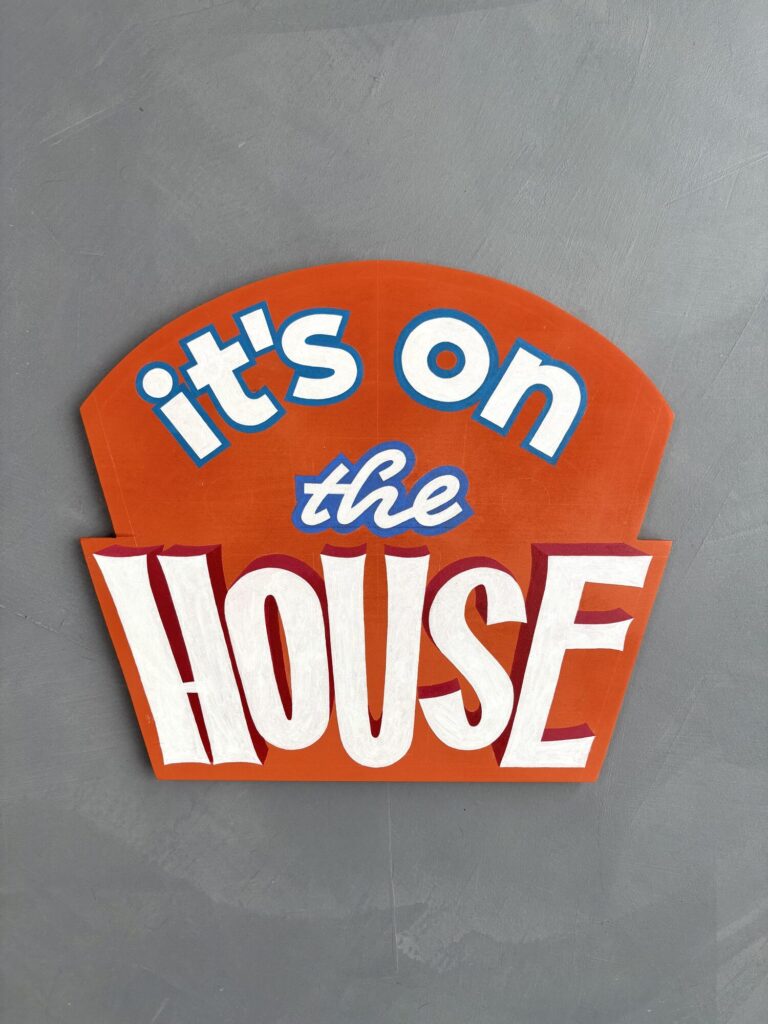 Orange and white It’s on the House cut-out sign on a grey wall