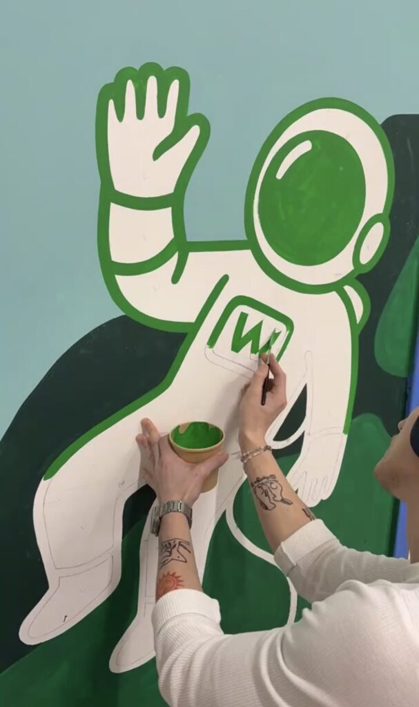 Torin painting a cartoon astronaut detail on the Partner Hub mural