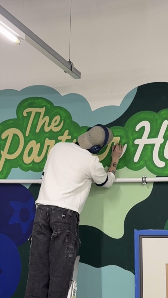Torin painting The Partner Hub script lettering on a green wall