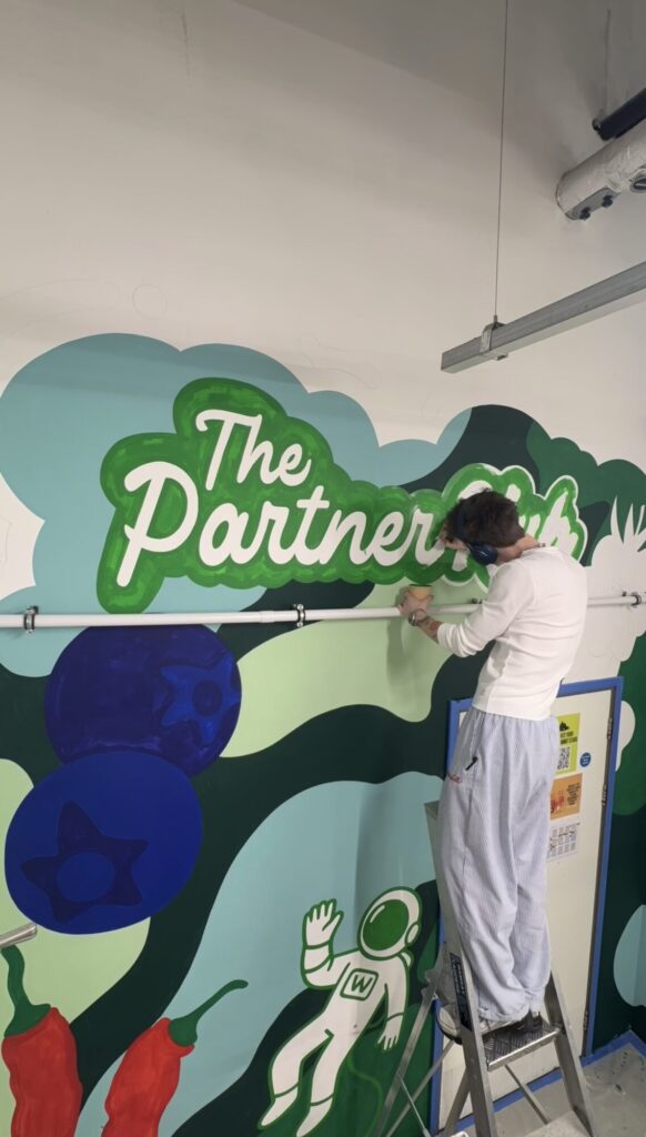 Torin on a ladder hand-lettering The Partner Hub across the mural