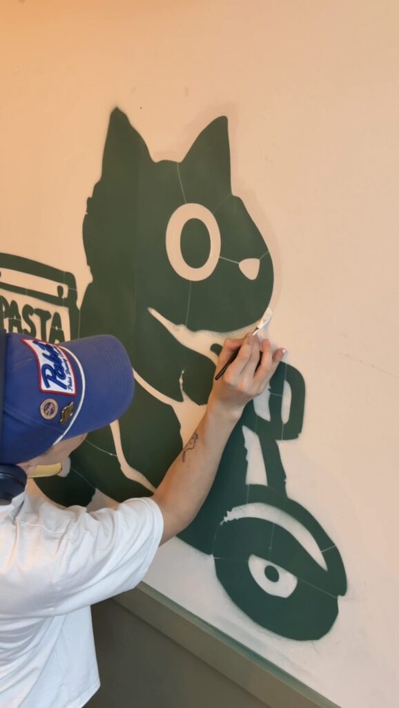Torin painting the outline of the pasta cat mural by hand