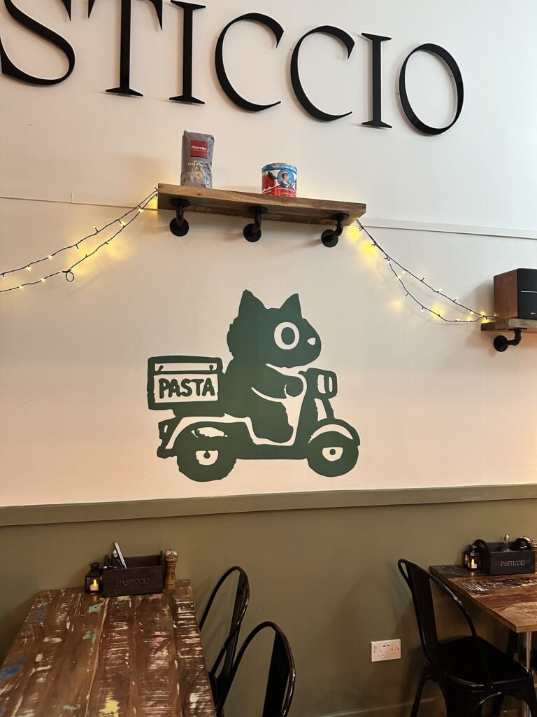 Green cat riding a pasta delivery scooter painted on the wall at Pasticcio