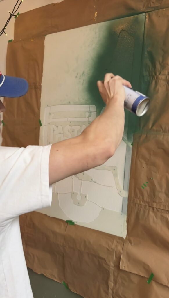 Spraying green paint through a stencil to block in the mural